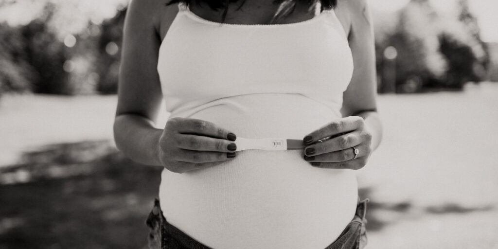 a pregnant woman holds a positive pregnancy test over her growing belly